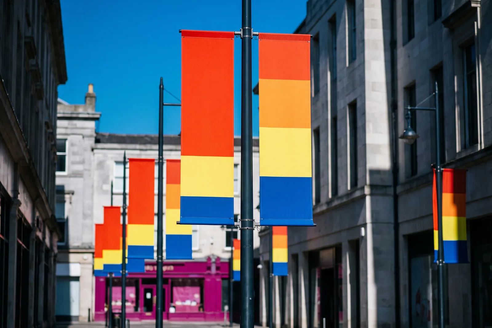 Orange, yellow and blue striped banner flags hanging from lampposts along a European stone-building street.